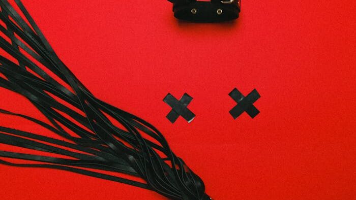 pexels-photo-5187498 Erotic BDSM accessories with leather choker and whip on striking red backdrop, emphasizing fetish themes.